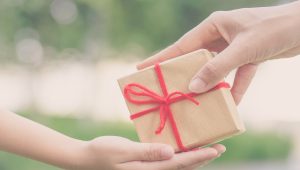 Holidays, present, christmas, childhood and happiness concept - close up of child and mother hands with gift box over green background. Vintage style.