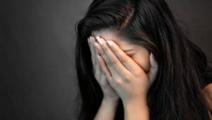 Close-up portrait of alone, stressed young woman sitting in darkness and crying with covering her face with hands.