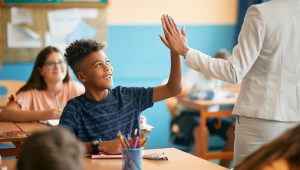Happy African American schoolboy giving high-five to his teacher during  class in the classroom.